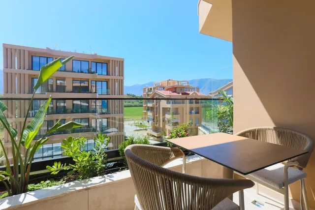 Balkon mit Tisch und Sesseln, dahinter Grün und Berge